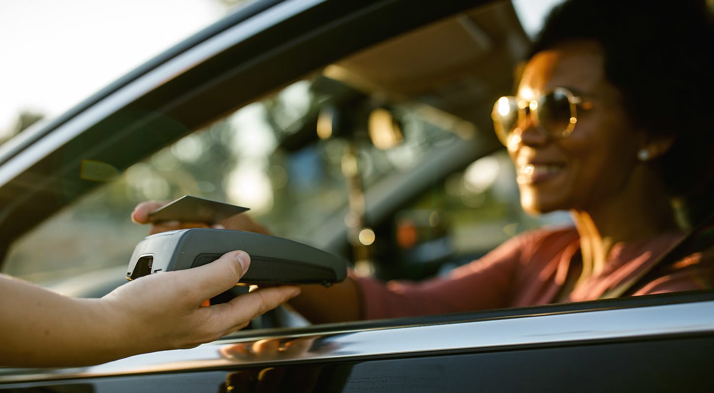 A woman seated in a car uses her credit card for tap to pay system at a drive-thru, illustrating the convenience of digital payments in contemporary banking.